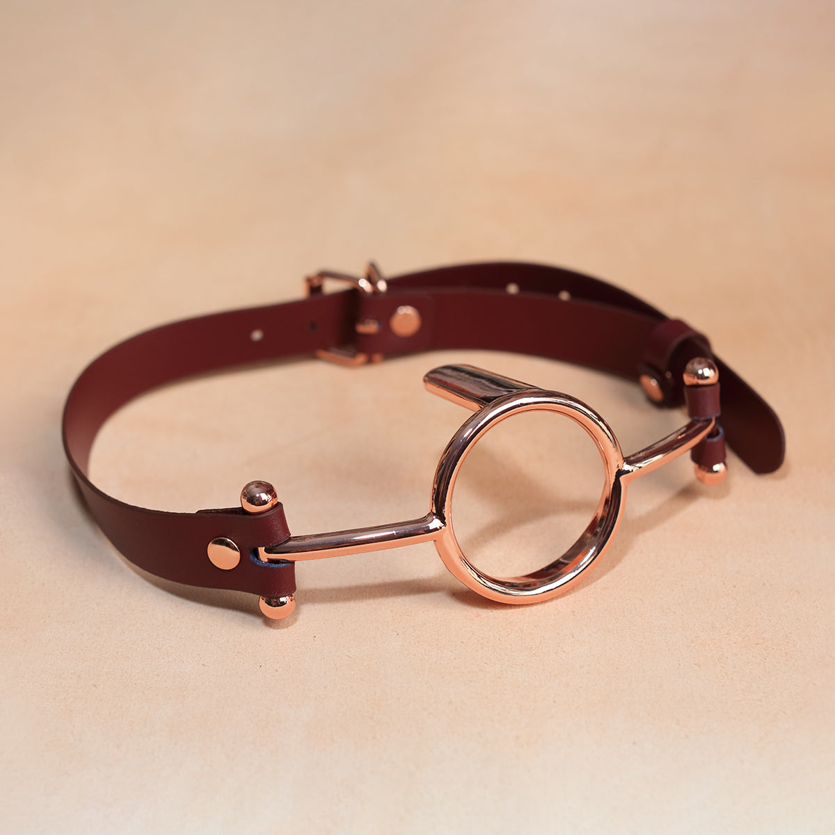 Close-up of luxurious gold metal O-ring tongue depressor gag with black premium vegan leather straps for oral bondage and deepthroat training by Sexy Maker.