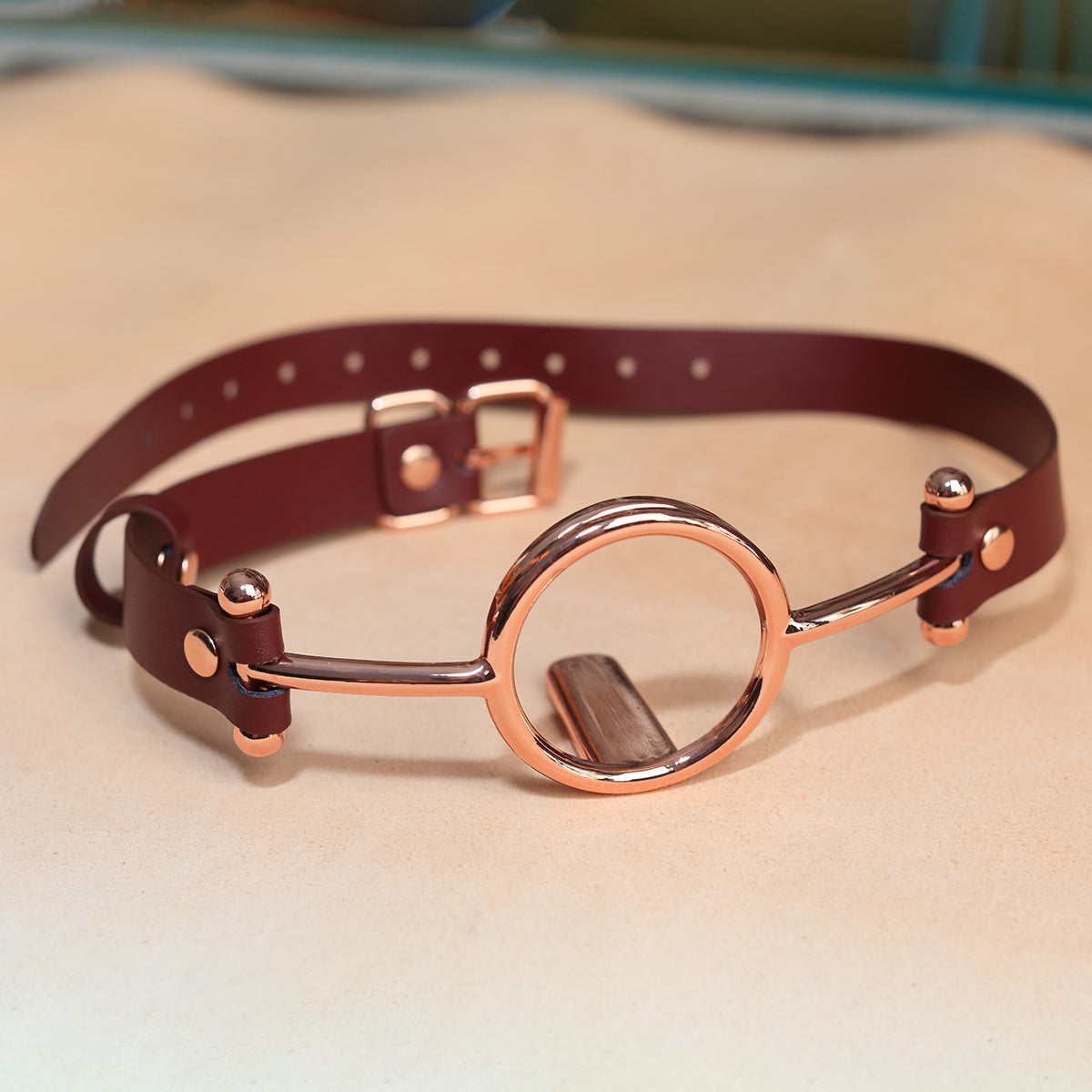 Close-up of luxurious gold metal O-ring tongue depressor gag with black premium vegan leather straps for oral bondage and deepthroat training by Sexy Maker.
