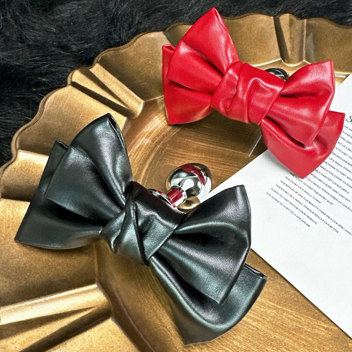 Front view of the Glossy Bow Anal Plug featuring a polished metal body and a black faux-leather ribbon, available on SexyMaker.